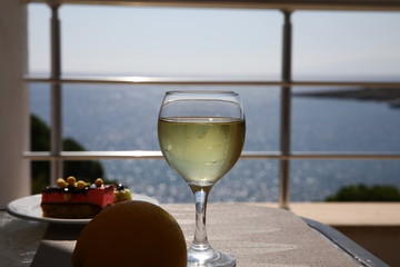 Cold white wine in a glass and a cake on a warm evening.Beautiful wine glass, water drops on the misted glass against the background of the Aegean sea.Selective focus on glass.Copy space for your text