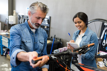 young apprentice making notes while mechanic works on bicycle