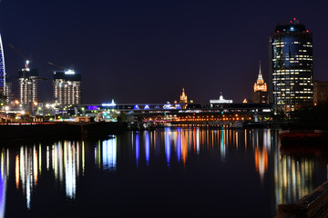Fototapeta premium brightly lit tall buildings at night and reflected in the river