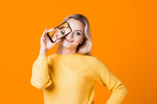 Cute young woman in a yellow sweater holding a smartphone