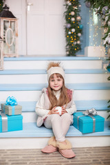 Merry Christmas, happy holidays! New Year 2020. little girl sits with gifts on porch of house decorated for Christmas. child sits on veranda decorated for New Year. Winter holidays concept. presents