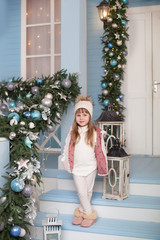 Merry Christmas, happy holidays! New Year 2020. little girl stands on porch of house decorated for Christmas. child decorates terrace for new year. Christmas decorated outdoor terrace with garlands.