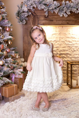 Merry Christmas, happy holidays! New Year. little girl is standing in a dress in bright New Year's interior. little child decorates Christmas tree. Happy kid is waiting for miracle and enjoys holiday.