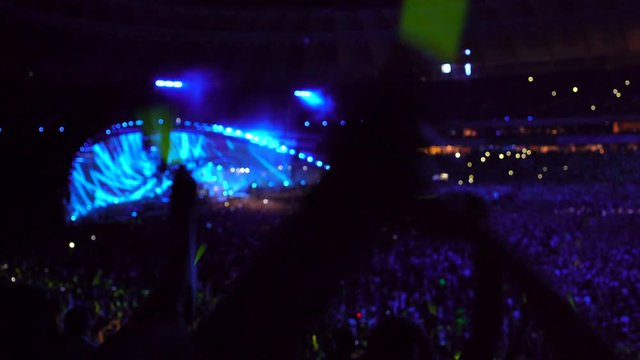 Big music concert at the stadium, people waving glow sticks