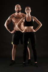 Fototapeta na wymiar Athletic man in shorts and sneakers with brunette woman in leggings and top posing on black background. Fitness couple, gym concept.