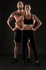 Fototapeta na wymiar Athletic man in shorts and sneakers with brunette woman in leggings and top posing on black background. Fitness couple, gym concept.