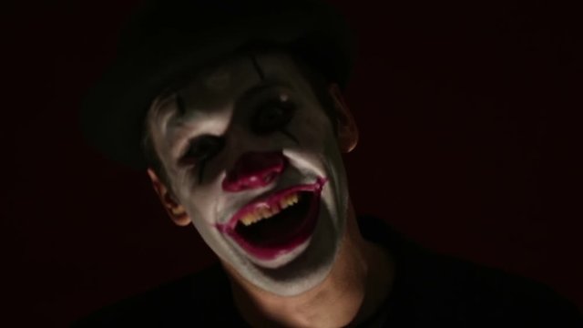 Scary man in a clown makeup looks at the camera and laughs. A scary clown looks at the camera and laughs terribly.Scary clown grimaces looking into camera .Halloween.