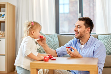 family, fatherhood and childhood concept - happy father and little daughter with toy crockery...