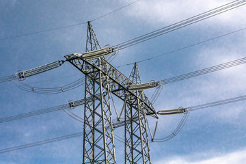 A low angle and off to the side view of a tall electric pylon, steel lattice architecture used to support overhead power cables, against clouds with copy-space.