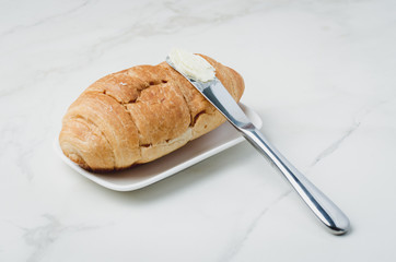 Croissant and a knife with butter on a white stone table. French breakfast
