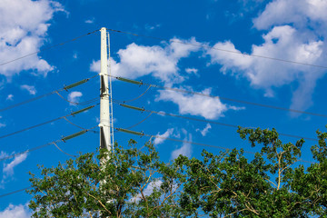 A low angle view of an electric pylon against a summer sky scene with green tree tops in the...
