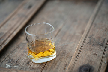 Detail of beautiful whisky glass with golden shimmering whisky on a rustic wooden used barrel