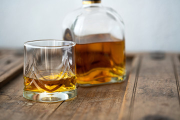 Glass and bottle of golden shimmering whisky on wooden table
