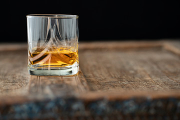 Shimmering glass of golden whisky on a wooden table in front of black background