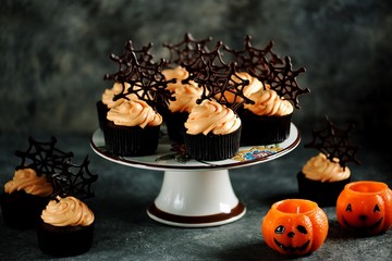 Chocolate cupcakes with pumpkin cream and chocolate spider web. Dessert for Halloween.