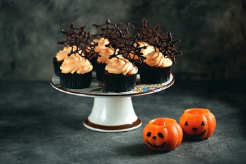 Chocolate cupcakes with pumpkin cream and chocolate spider web. Dessert for Halloween.