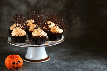 Chocolate cupcakes with pumpkin cream and chocolate spider web. Dessert for Halloween.