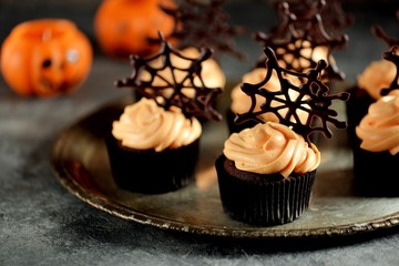Chocolate cupcakes with pumpkin cream and chocolate spider web. Dessert for Halloween.