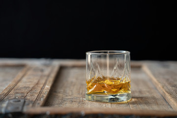 Beautiful whisky glass on used shabby wooden table in front of black background