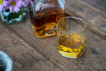 Close up of a whisky bottle and glass on old barrel with flower