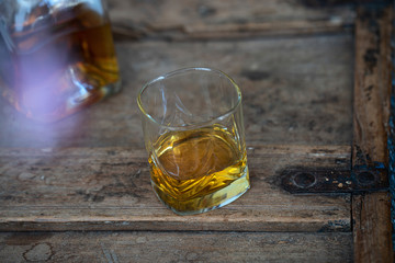 Glass and bottle of scotch on old oak barrel with reflection