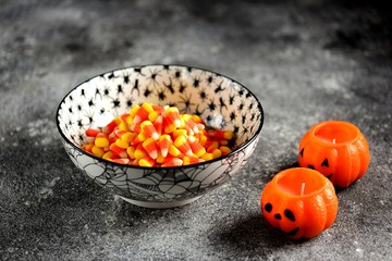 Halloween candy corn in a traditional bowl with spiders pattern on a gray background.