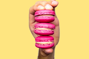 Hand, die drei rosa Macarons hält. Nahaufnahme der Kekse. Gelber Hintergrund. Isoliertes Thema