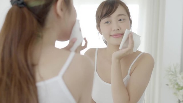 Beautiful young asian woman smile with skin care use oil blotting paper on face looking mirror in the bathroom, beauty asia girl happy and cheer makeup and cosmetic, health care on facial concept.