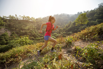 Naklejka na ściany i meble Woman ultramarathon runner running up on mountain slope in tropical forest