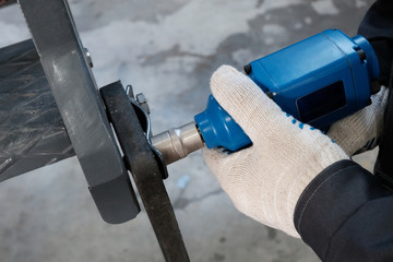 A technician tightens the bolt with an electric tool. Close-up of male hands tightening a nut on a metal product. Gun for twisting.