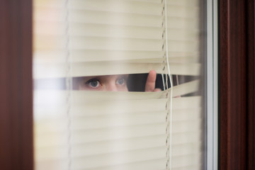 woman looking through window blinds into the street waiting