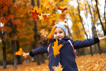 Portrait of cheerful children playing with yellow and orange dry autumn leaves.