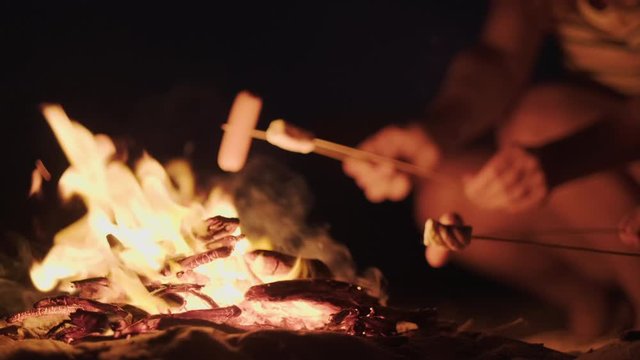 Tourists fry sausages, marshmallows over high heat, flames at late beautiful sunset of the day, close-up. Family at the campsite relax on summer vacation by the sea and cook. Family. Lifestyle. 