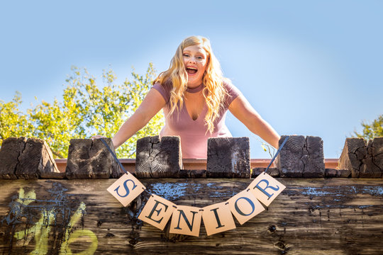 Teen girl poses for a high school senior portrait photo outdoors on a bridge with a sign saying Senior