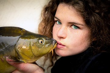 Young woman with impressive green eyesvkissing a carp, fish