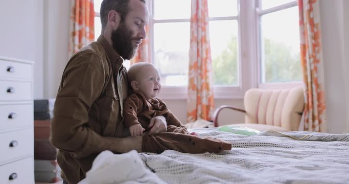 Single father dressing baby on bed in bedroom