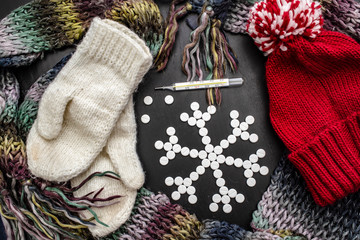 Concept snowflakes made from medical pills lies next to colorful winter clothes and a thermometer.
