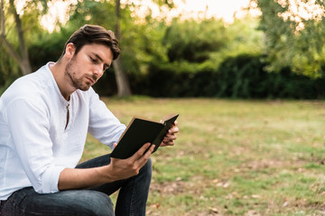 Young man sitting in a park carefully reads an old book.