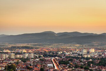 Beautiful golden hour sky above Pirot cityscape with buildings lighten by setting sun, city lights and car trails