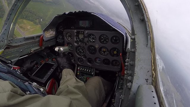 The pilot hold and control helm. Gray training aircraft is heading for the target. A fighter fly low over a river and green fields against a dark cloudy sky. View of cockpit and dashboard close up.
