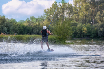 Man wakeboarding on river lake sea on summer spring day in jacket. Soft focus. Action blur.
