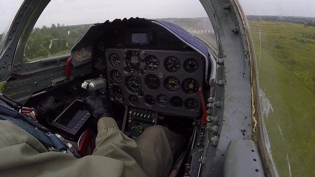 Hand of pilot hold and control helm. Gray fighter plane go down on the landing strip or runway of old airfield against a dark cloudy sky. The aircraft is touching the ground. View of cockpit close up.