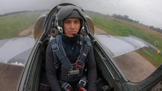 The second pilot correct helmet and looks around. Gray blue fighter combat aircraft move the runway at old airfield on a cloudy day. Inside view of cockpit. The plane drive on concrete slabs.