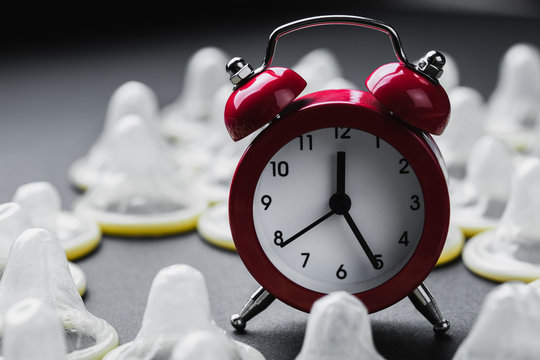 red alarm clock with condoms on black background