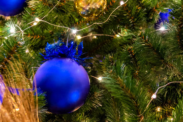 Christmas toys, balls of blue and gold colors, shining garland on the Xmas tree. Close-up