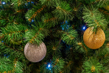 Christmas toys, balls of gold and silver colors, a shining garland hanging on the branch of the Xmas tree. Close-up.