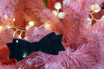 Xmas decorations. Pink branches of the Christmas tree. Decorated with garland and toy in the form of bow-tie . Custom design. Close-up