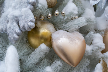 Christmas decorations. A spruce branch of unusual white color, decorated with toys in the form of a heart and a ball, gold color. Covered in snow. Close-up
