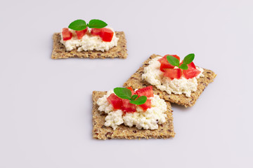 Diet flax seed whole grain crackers with ricotta cheese, tomato and herbs isolated on white background, soft light