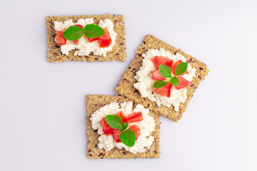Diet flax seed whole grain crackers with ricotta cheese, tomato and herbs isolated on white background, soft light
